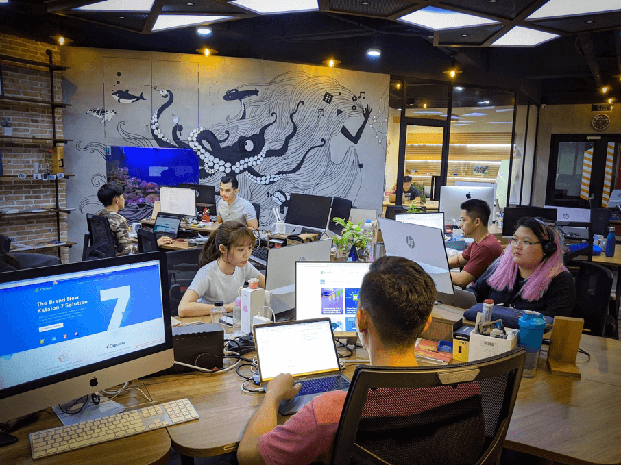 People sit in an office working at their computers. A large mural of a squid is painted on the wall behind the employees. 